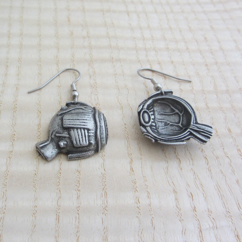 May include: A pair of silver earrings shaped like a fish with a detailed design. The earrings are hanging from silver hooks.