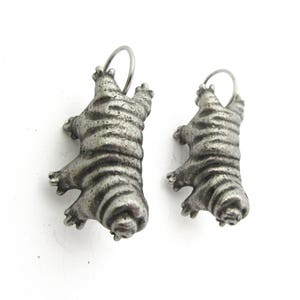 May include: A pair of silver-toned metal pendants shaped like tardigrades, also known as water bears. Each pendant features a segmented, textured body with eight distinct legs and a small circular loop at the top for attachment to a chain or cord.