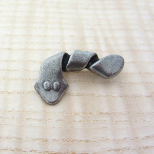 May include: A decorative, antique-style metal drawer pull with a twisted ribbon design. The pull features a gray, textured finish and a diamond-shaped base with two small, round details. The design is reminiscent of vintage hardware.