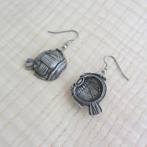 May include: A pair of silver earrings shaped like a human eye. The earrings are detailed and realistic, with the iris, pupil, and sclera all visible.