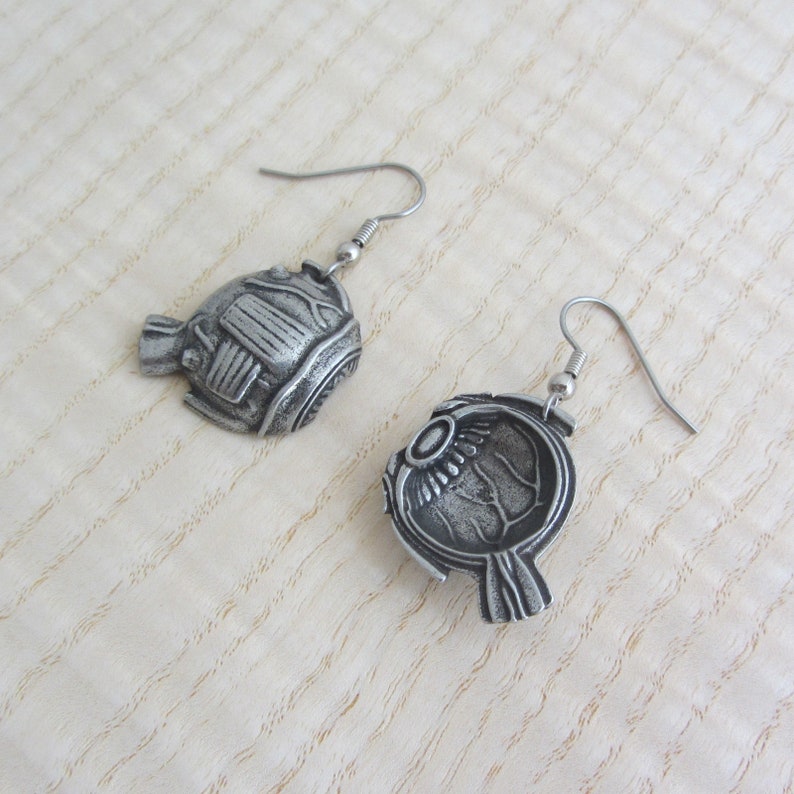 May include: A pair of silver earrings shaped like a human eye. The earrings are detailed and realistic, with the iris, pupil, and sclera all visible.