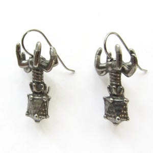 May include: A pair of silver earrings featuring a scorpion design with a geometric, faceted gemstone at the bottom.