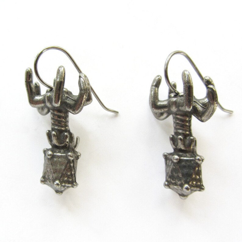 May include: A pair of silver earrings featuring a scorpion design with a geometric, faceted gemstone at the bottom.