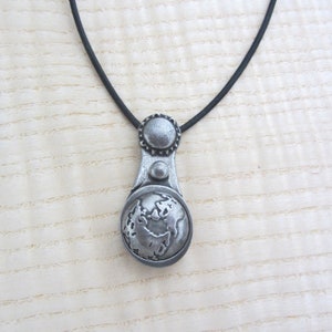 May include: A silver necklace with a pendant featuring a detailed globe design. The pendant has a textured surface and a small circle on the top.