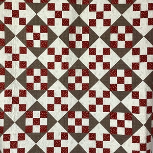 May include: A quilt with a geometric pattern of red and brown squares. The quilt is made of fabric with a small white polka dot pattern.