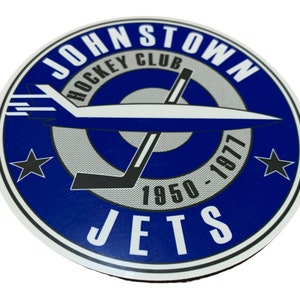 May include: A circular sticker featuring the words "Johnstown Hockey Club" and "Jets" in white text on a blue background. A stylized airplane and hockey stick are in the center. The years "1950-1977" are also displayed.
