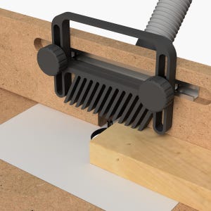 Puede incluir: Un jig de router de plástico negro con una valla en forma de peine y dos botones ajustables. El jig está unido a una mesa de router y se está utilizando para cortar una pieza de madera.