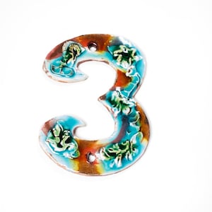 May include: A blue and brown ceramic number three with floral details. The number is a decorative piece for a home.
