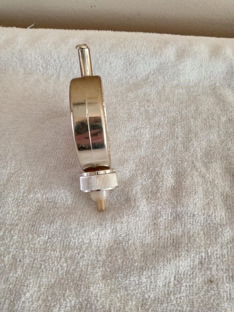 Pu&ograve; includere: Un tappo per bottiglia di vino in metallo argentato con un corpo a forma di anello e una parte superiore cilindrica. Il tappo ha una base filettata scanalata e un piccolo beccuccio conico. L'oggetto &egrave; su una superficie bianca e strutturata.