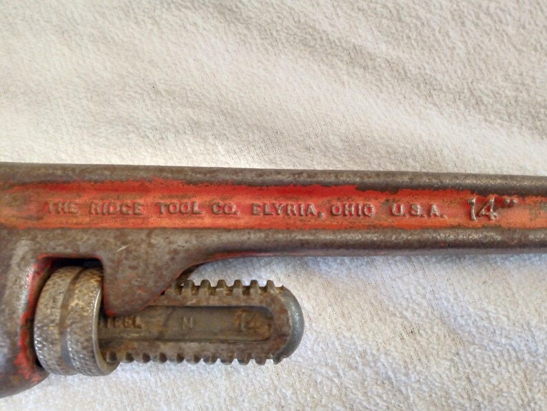 Op de afbeelding: Een vintage pijpsleutel van 35,56 cm van The Ridge Tool Co. in Elyria, Ohio, VS. De sleutel is voornamelijk roestig oranje met zichtbare tekst en een getande bek voor het vastgrijpen van pijpen. De tool vertoont slijtage.