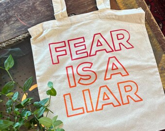 May include: A white canvas tote bag with the text "FEAR IS A LIAR" printed in red and orange.