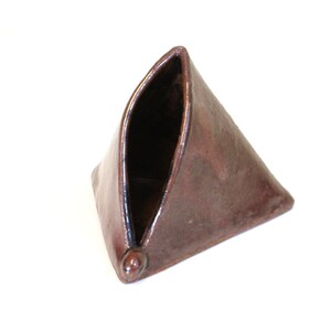 May include: A small, triangular ceramic vase with a brown glaze. The vase has a folded design, creating a unique shape.