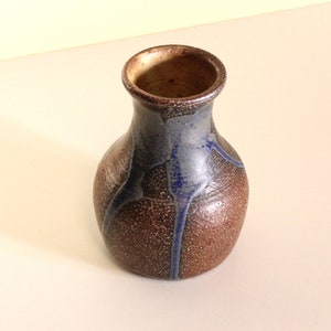 May include: A small, brown ceramic vase with blue glaze accents. The vase has a rounded body and a narrow neck.