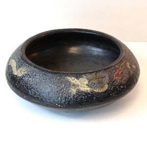 May include: A black ceramic bowl with a textured surface and gold and red painted designs. The bowl features a stylized dragon design.