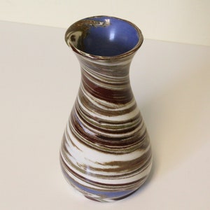 May include: A ceramic vase with a swirling pattern of brown, white, and blue glaze. The vase has a narrow neck and a rounded base.