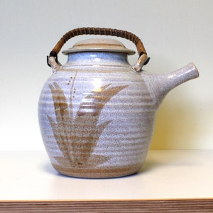 May include: A white ceramic teapot with a brown floral design and a woven handle.
