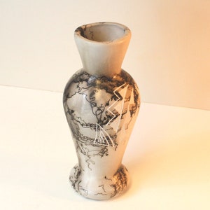 May include: A white ceramic vase with a black and white geometric design. The vase has a narrow neck and a wide base.