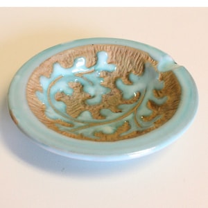 May include: A small, light blue ceramic ashtray with a brown leaf design.