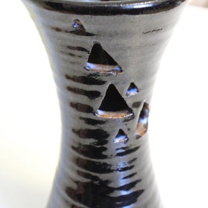 Puede incluir: Jarrón de cerámica negro con una superficie texturizada y tres recortes triangulares. El jarrón tiene un cuello estrecho y una base ancha.