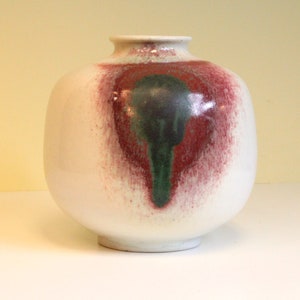 May include: White ceramic vase with a red and green abstract design. The vase has a round body and a wide opening.