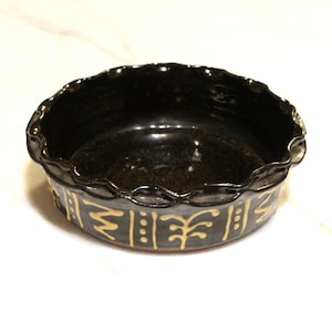 May include: A black ceramic bowl with a scalloped rim and gold geometric designs. The bowl is perfect for serving snacks or dips.