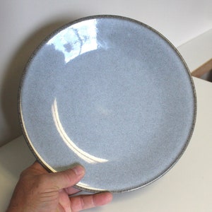 May include: A light gray ceramic dinner plate with a slightly textured surface and a dark gray rim.