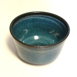 May include: A small, teal blue ceramic bowl with a dark brown rim. The bowl has a slightly textured surface.
