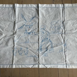 May include: A white fabric with blue embroidery depicting a windmill, a woman in a dress, and three geese. The embroidery is done in a simple, folk art style.