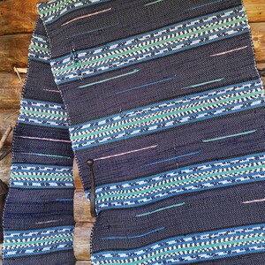 May include: A blue and white woven rug with a geometric pattern. The rug is hanging on a wooden wall.