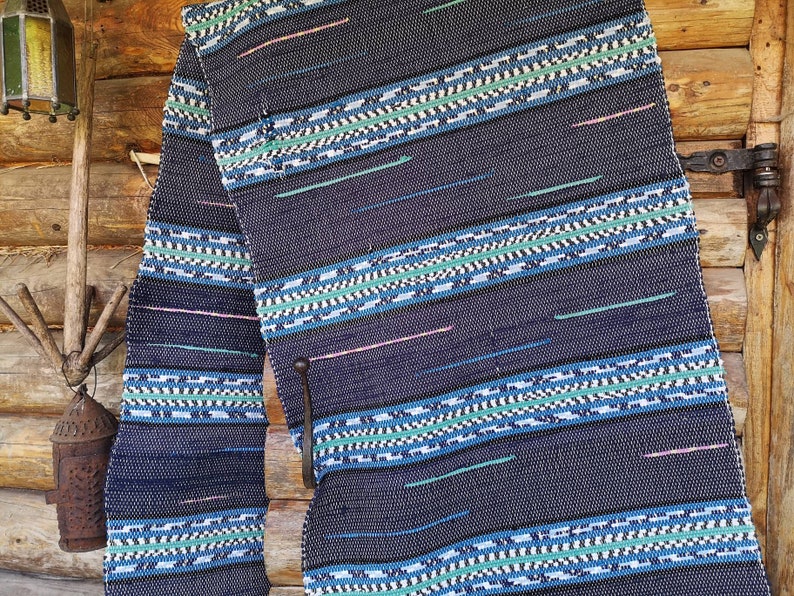 May include: A blue and white woven rug with a geometric pattern. The rug is hanging on a wooden wall.