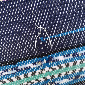 May include: Close-up of a blue and white woven rug with a white thread detail. The rug has a geometric pattern with blue, white, and green stripes.