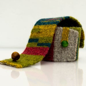 May include: A small box with a lid made of felted wool. The box is decorated with stripes of green, yellow, red, and blue wool. The lid is folded over the box and a small green button is attached to the lid.