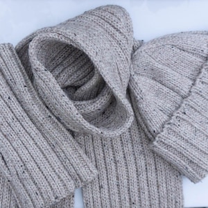 May include: A beige knitted scarf and beanie set. The scarf is folded and the beanie is lying on top of it.