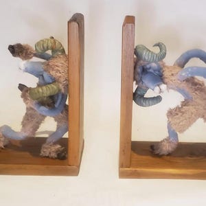 Könnte beinhalten: Ein Paar skurriler Buchstützen mit Figuren von Fabelwesen. Jede Buchstütze hat einen Holzsockel und eine aufrechte Stütze. Die Kreaturen sind blau mit braunem Fell und grünen Hörnern und scheinen zu rennen.