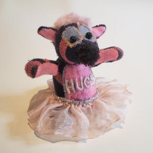 May include: A pink and black sock monkey wearing a pink tutu with the word "HUGS" embroidered on the front.