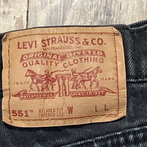 Puede incluir: Un parche de cuero marrón Levi Strauss & Co. con costuras rojas. El parche tiene el logotipo de la empresa, "Original Riveted Quality Clothing", y el texto "551™ Relaxed Fit Tapered Leg W L".