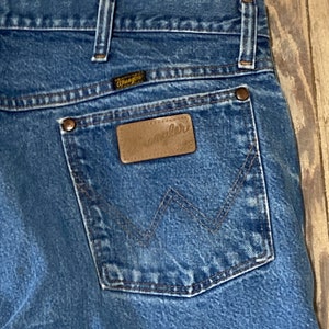 May include: A pair of blue denim jeans with a brown leather back pocket patch that says "Wrangler".