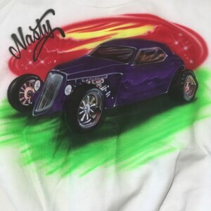 May include: A white sweatshirt with a purple hot rod car airbrushed on the front. The car is surrounded by a red, yellow, and green flame design. The word "Nasty" is written in black above the car.