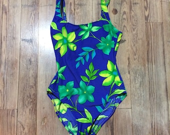Pode incluir: Um maiô azul com estampa floral com flores verdes e amarelas. O maiô tem um decote redondo e alças finas.