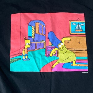 May include: A black t-shirt with a graphic print of Marge Simpson from The Simpsons, dancing with her arms raised, while Bart Simpson stands in the background. The text "Simpsons" is printed in the bottom right corner of the graphic.
