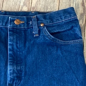 May include: Close-up of the top of a pair of blue denim jeans with a copper button and rivets. The jeans have a classic five-pocket style.