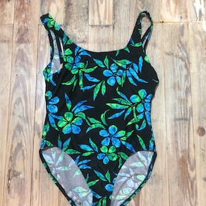 May include: A black swimsuit with a green and blue floral print. The swimsuit has a scoop neck and thin straps.