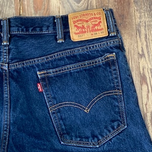 May include: A pair of blue denim jeans with a brown leather Levi Strauss & Co. patch on the back waistband. The patch has the text "Levi Strauss & Co." and "Original  Riveted Quality Clothing" with a horse and rider logo. The patch also has the text "517" and "W 38 L 30".