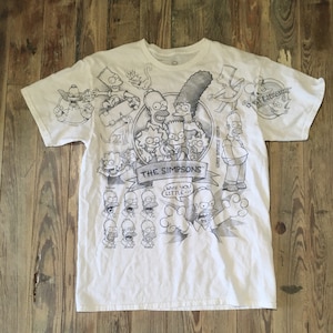 May include: White t-shirt with a black and white print of various Simpsons characters, including Homer, Marge, Bart, Lisa, Maggie, and others. The text "The Simpsons" and "Why you little..." are printed on the shirt.