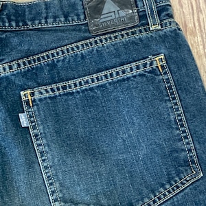 May include: A pair of blue denim jeans with a back pocket and a leather patch that says "Silvertire" on the back waistband.