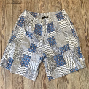 Könnte beinhalten: Patchwork-Shorts mit weißem Hintergrund und blauen und orangefarbenen Blumenmustern. Die Shorts haben einen Knopf- und Reißverschluss.
