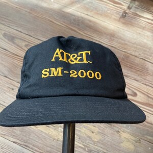 May include: A black baseball cap with a gold embroidered logo that says "AT&T SM-2000".
