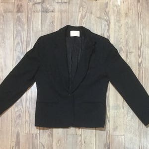 Puede incluir: Una chaqueta negra con un cierre de botón único y solapa de muesca.