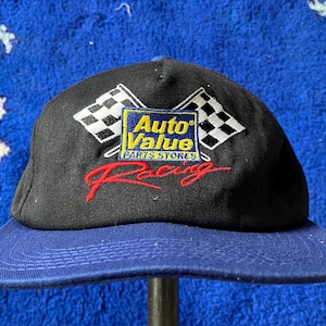 Könnte beinhalten: Eine schwarze und blaue Baseballkappe mit einer weißen karierten Flagge und den Worten "Auto Value Parts Stores" bestickt auf der Vorderseite. Die Kappe hat auch das Wort "Racing" in Rot bestickt.