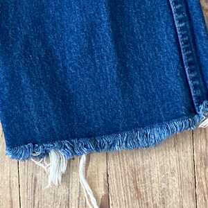 May include: Close-up of the frayed hem of a pair of blue denim jeans.